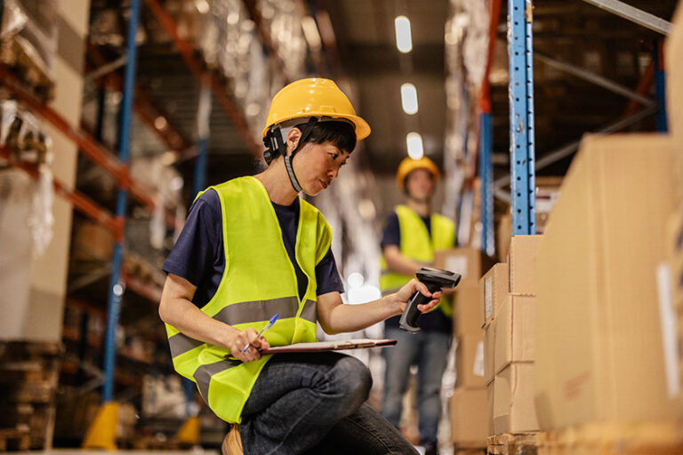 A focused Asian warehouse worker scanning boxes